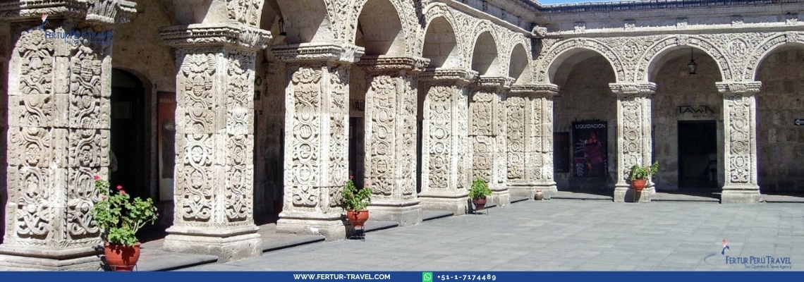 Ornate white sillar stone arches with intricate baroque carvings at the Yanahuara viewpoint in Arequipa, Peru, with potted flowers along the colonnade